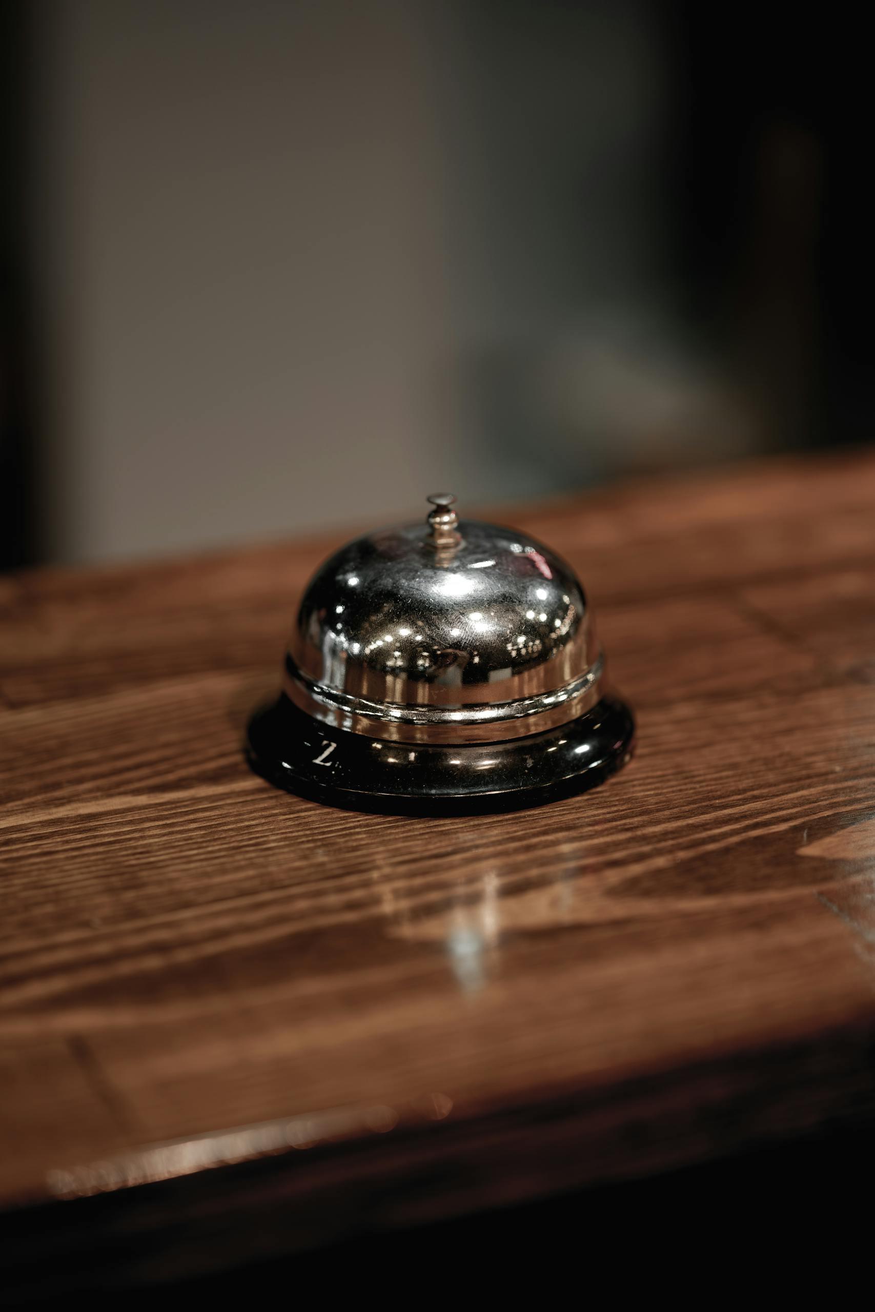 A shiny metal hotel bell on a polished wooden counter, ideal for hospitality themes.
