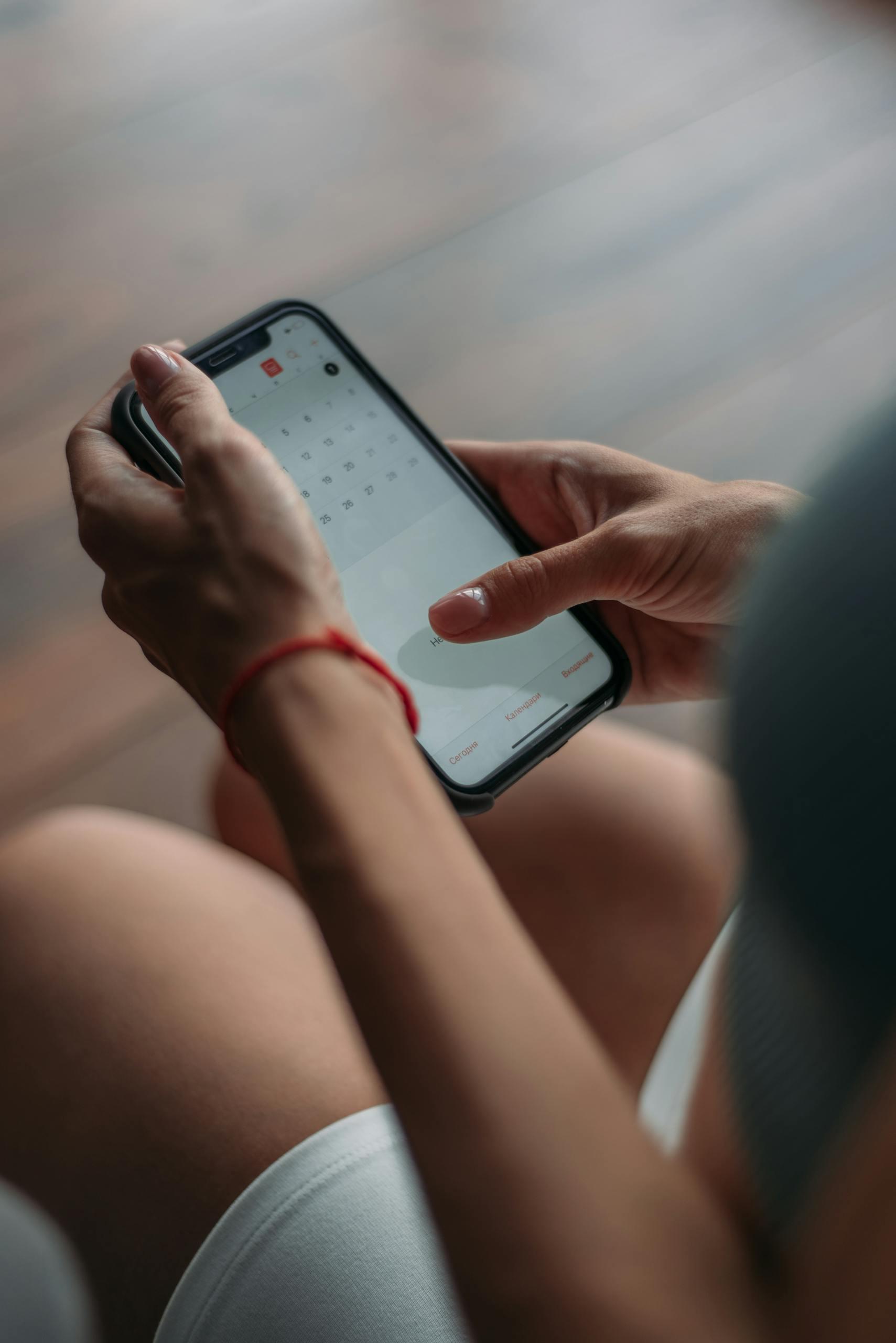 Close-up of a person using a smartphone to access the calendar for making a booking